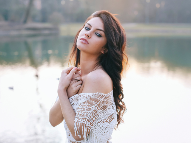 Красивая девушка в белом наряде стоит у озера