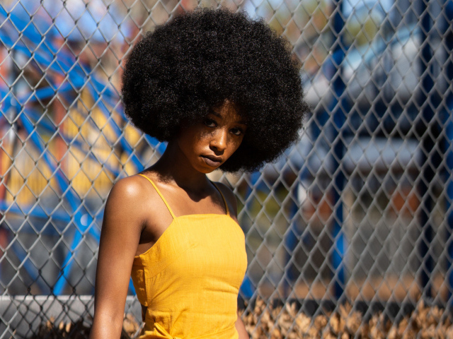 Темнокожая девушка в желтом платье стоит у сетки