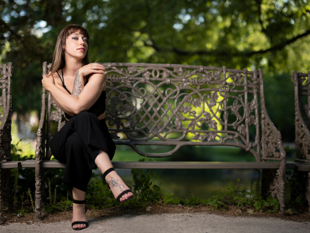 Девушка в черном костюме сидит на лавке 