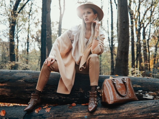 Девушка в пальто сидит на упавшем дереве в лесу 