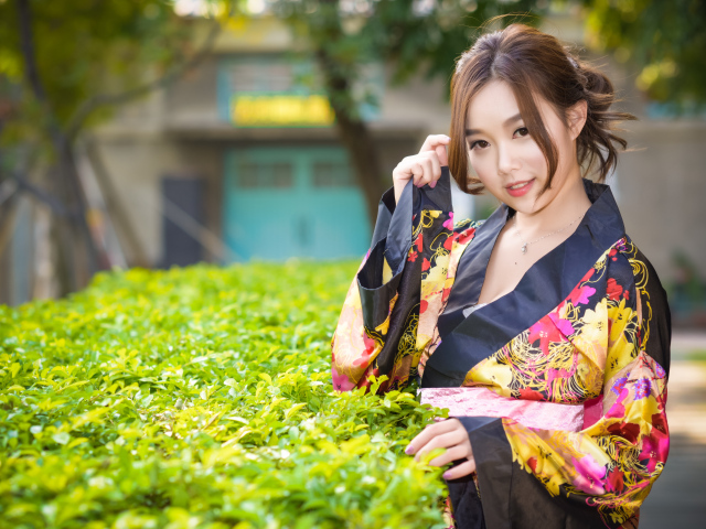 Девушка в кимоно стоит у зеленого куста