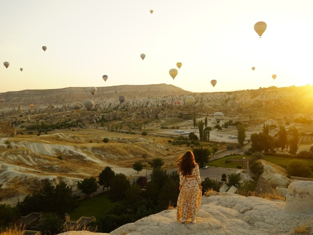Девушка стоит на краю скалы на фоне неба с воздушными шарами