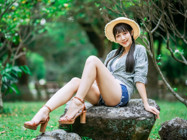 Девушка азиатка в шляпе сидит на камне