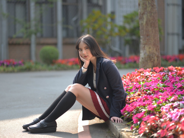 Девушка азиатка  сидит на клумбе с цветами