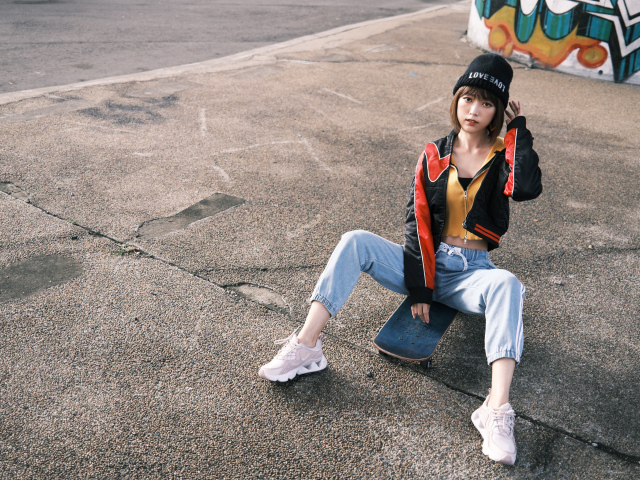 Девушка азиатка сидит на скейтборде на асфальте 
