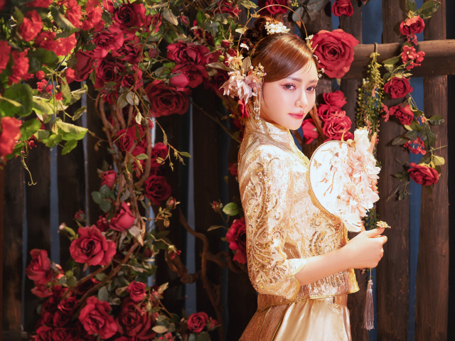 Азиатка в красивом национальном костюме у куста роз