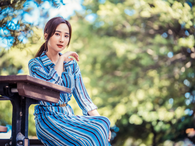 Красивая девушка азиатка в платье  за столом в парке 