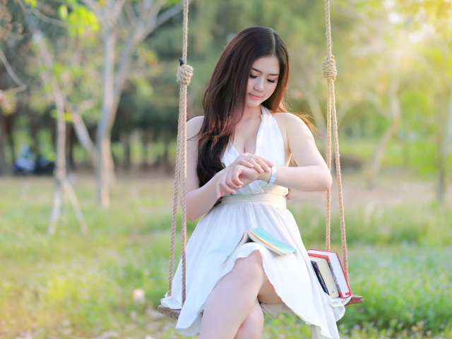 Красивая девушка азиатка в белом платье сидит на качели