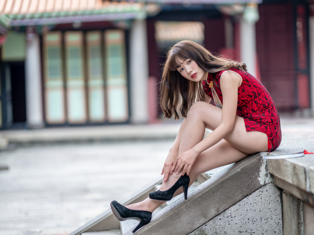 Красивая девушка азиатка в красном платье сидит на ступеньках