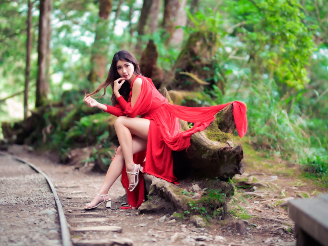 Красивая азиатка в красном платье сидит на дереве 