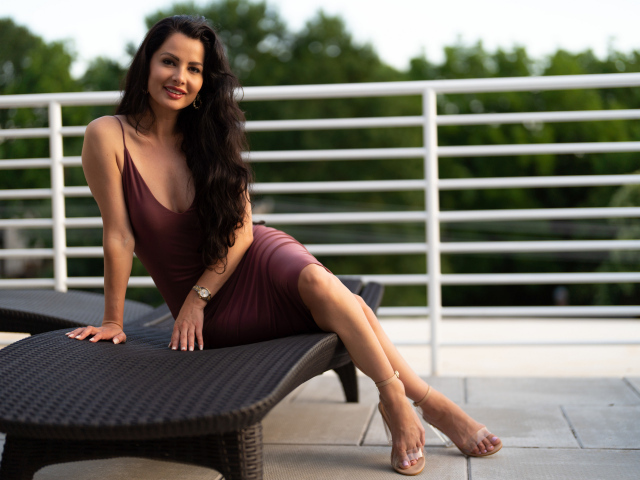 Красивая брюнетка в платье сидит на диване 