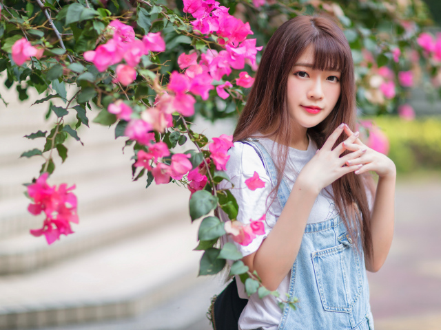 Красивая милая азиатка стоит у куста с розовыми цветами
