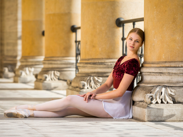 Красивая девушка балерина сидит на полу у колонны 