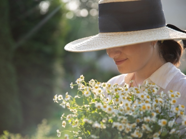 Красивая девушка в шляпе с букетом ромашек 