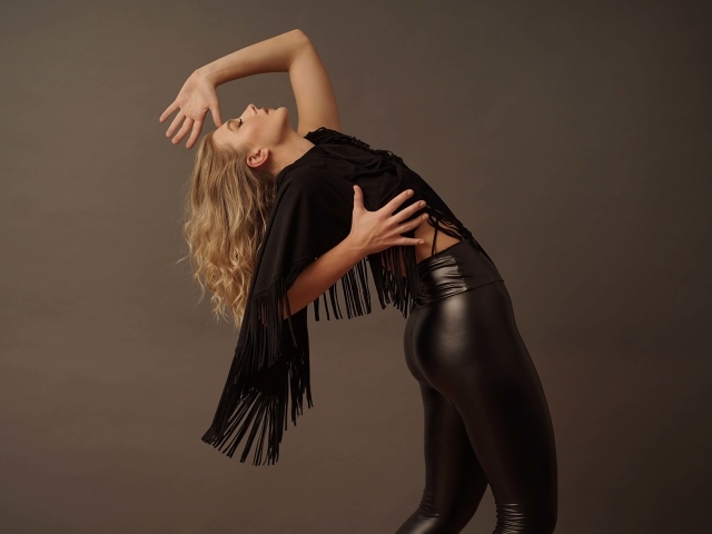 Красивая девушка в черных кожаных брюках на сером фоне