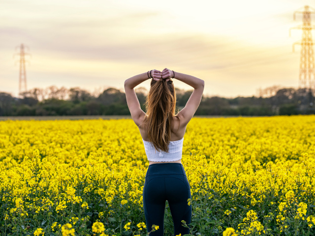 Красивая девушка стоит на поле с рапсом