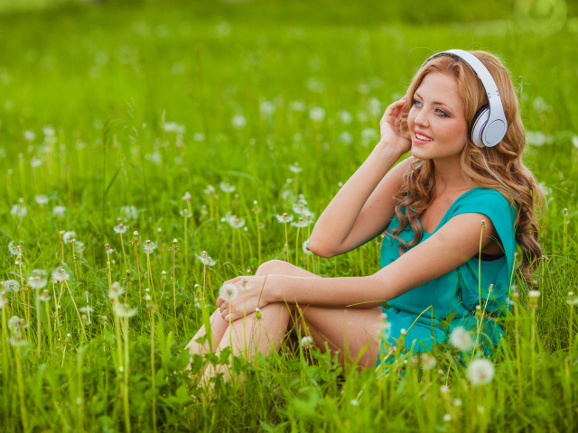 Красивая девушка с наушниками на голове  сидит на траве