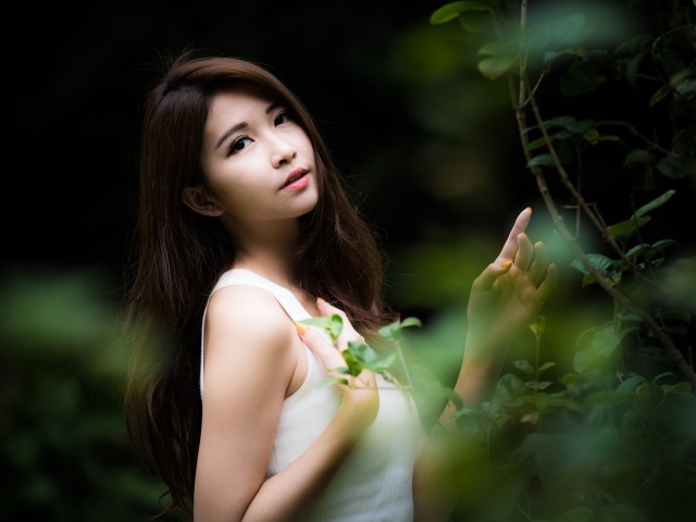 Милая азиатка в белом стоит у зеленых листьев