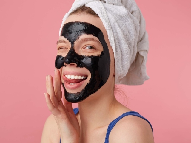 Смешная молодая девушка с черной косметической маской на лице 