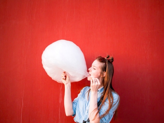 Девушка ест сладкую вату на красном фоне 