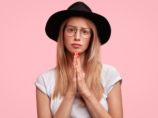 Девушка в черной шляпе на розовом фоне просит прощения