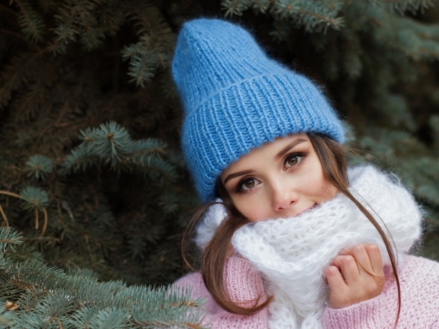 Девушка в голубой вязаной шапке у ели