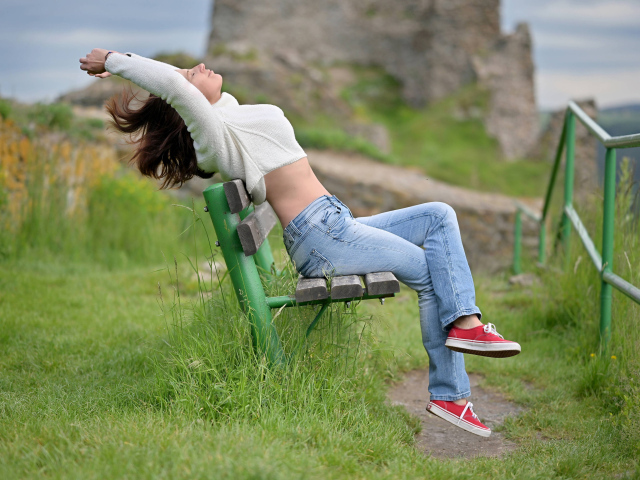 Девушка в синих джинсах сидит на лавке 