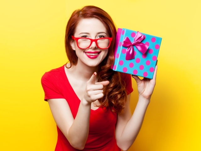 Девушка в очках с подарком в руке на желтом фоне