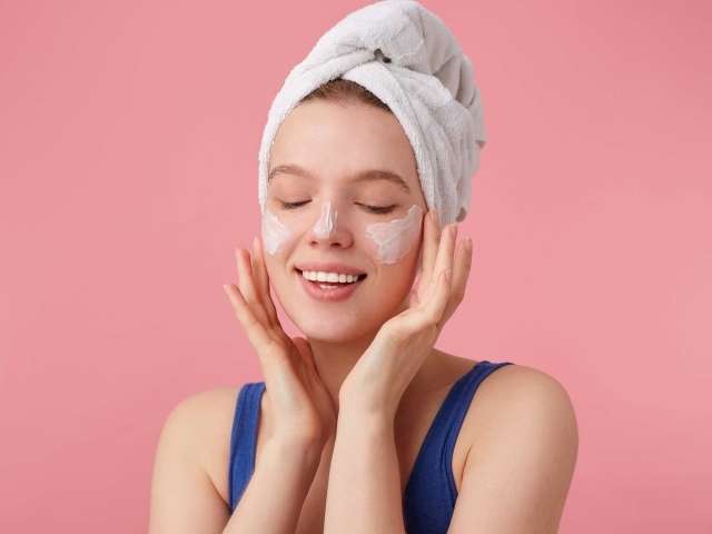 Девушка с полотенцем на голове мажет крем на лицо