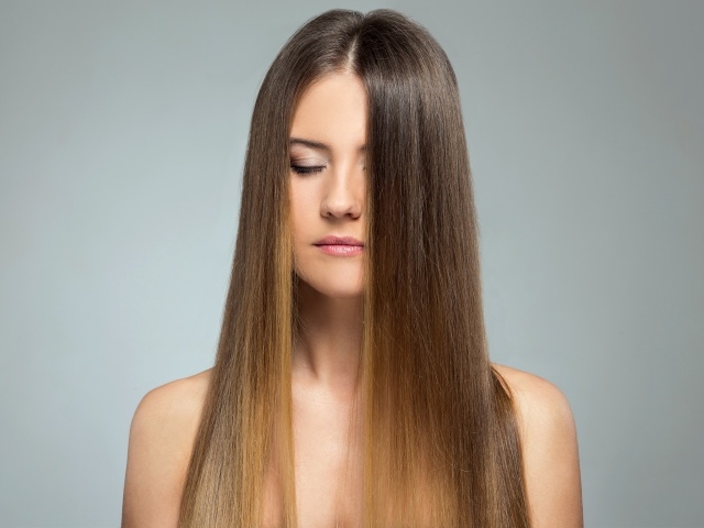 Длинноволосая шатенка с закрытыми глазами на сером фоне 