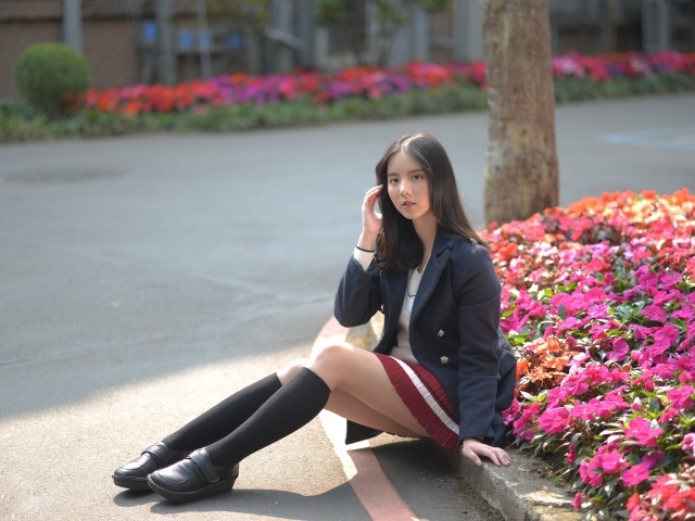 Девушка школьница сидит на земле у клумбы 