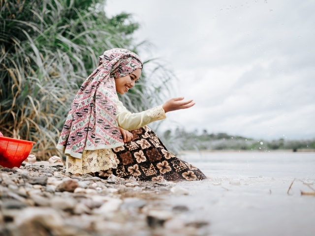 Улыбающаяся девушка азиатка сидит у воды