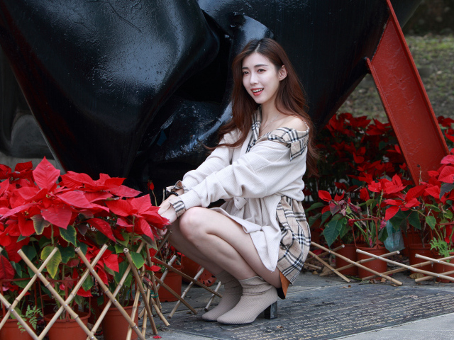 Улыбающаяся азиатка сидит у красных цветов 