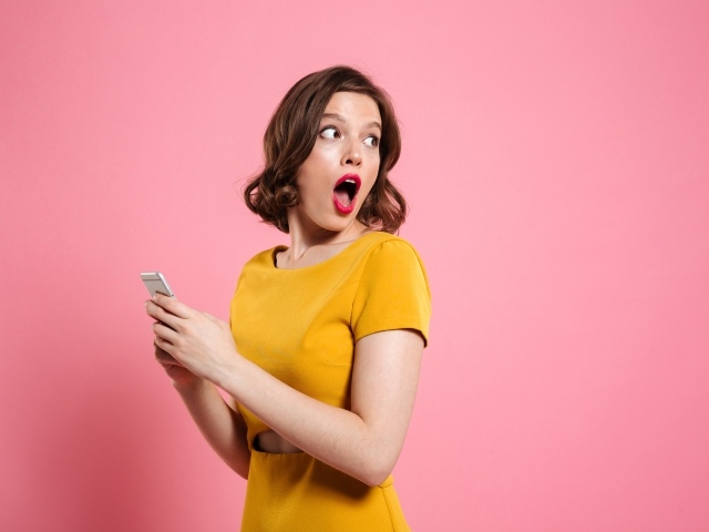 Удивленная девушка с телефоном в руках на розовом фоне