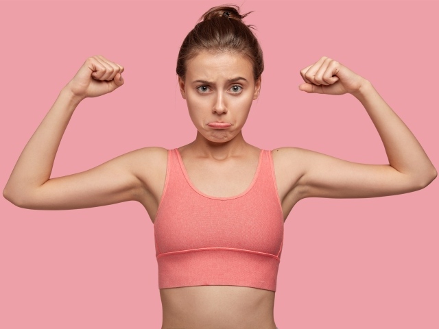 Расстроенная девушка без накаченных рук на розовом фоне