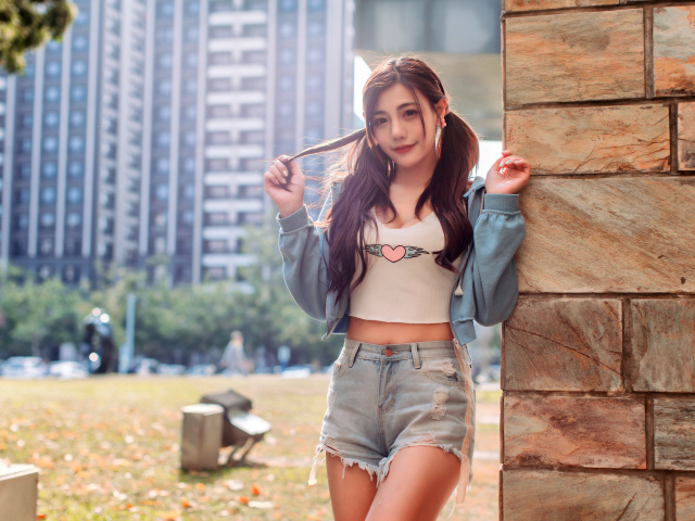 Молодая азиатка в коротких шортах стоит у стены