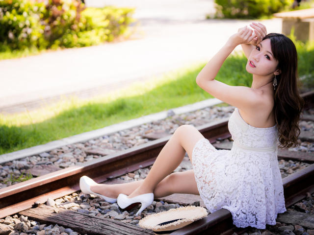 Молодая азиатка в белом платье сидит на рельсах 