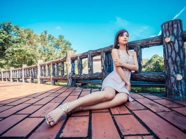 Молодая красивая азиатка сидит  на полу у забора