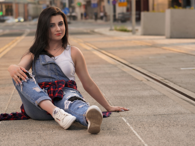 Молодая девушка в джинсовом наряде сидит на асфальте