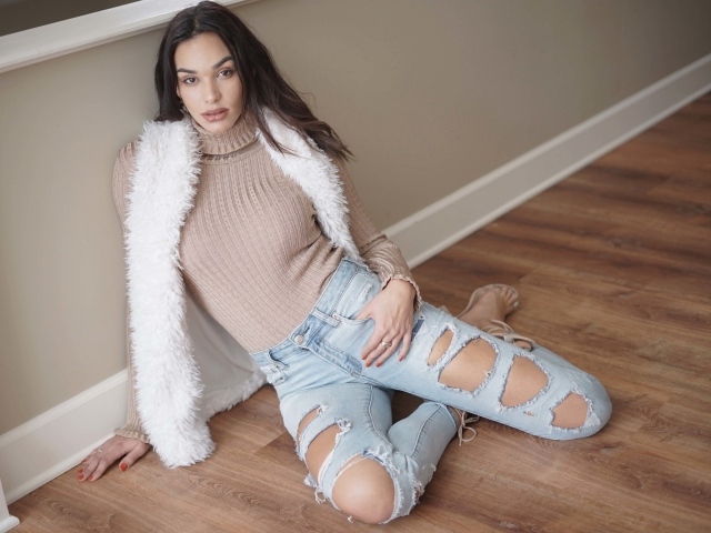 Молодая девушка в рваных джинсах сидит у стены