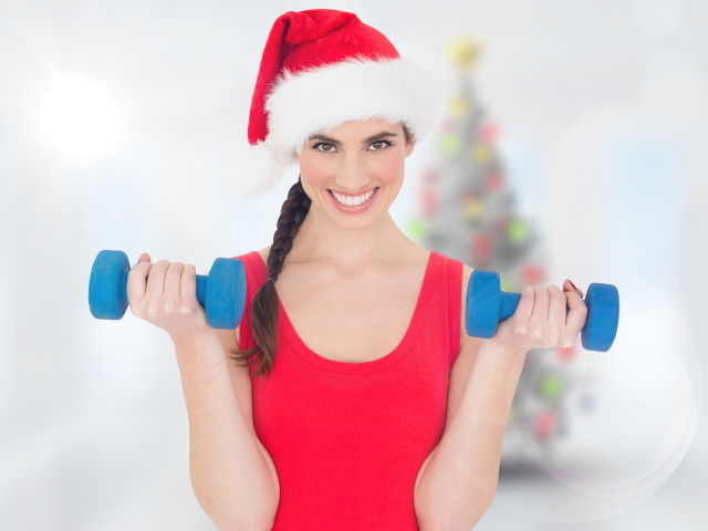 Красивая девушка в шапке Санта Клауса с гантелями в руках 