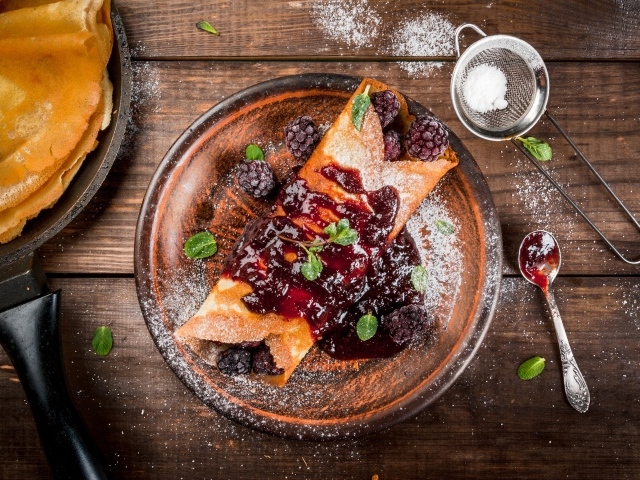 Блин с ягодами и джемом на тарелке с сахарной пудрой