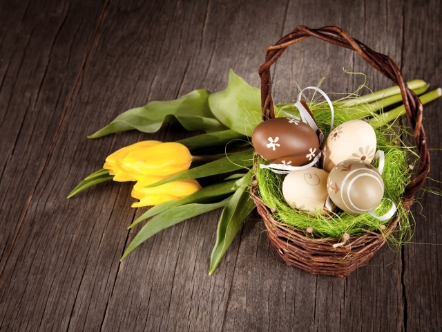 Маленькая корзина с пасхальными  яйцами на столе с тюльпанами