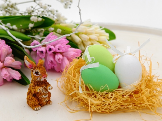 Три пасхальных яйца в гнезде на столе с цветами