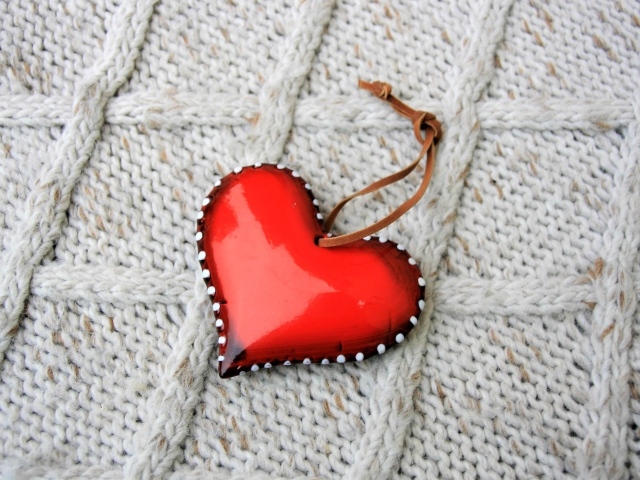 Красное сердце лежит на вязаном свитере 