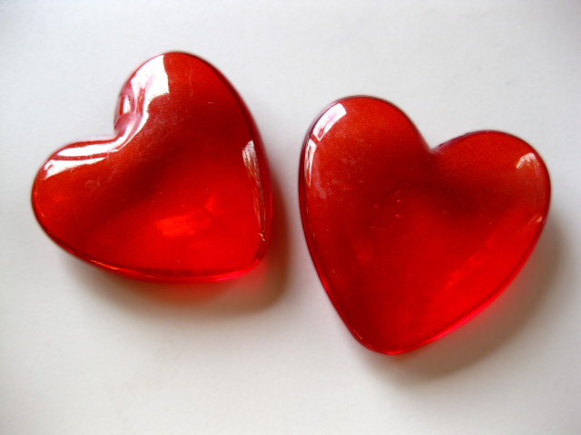 Два красных стеклянных сердца на сером фоне