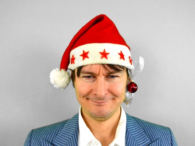 Голубоглазый мужчина в новогодней шапке на сером фоне 