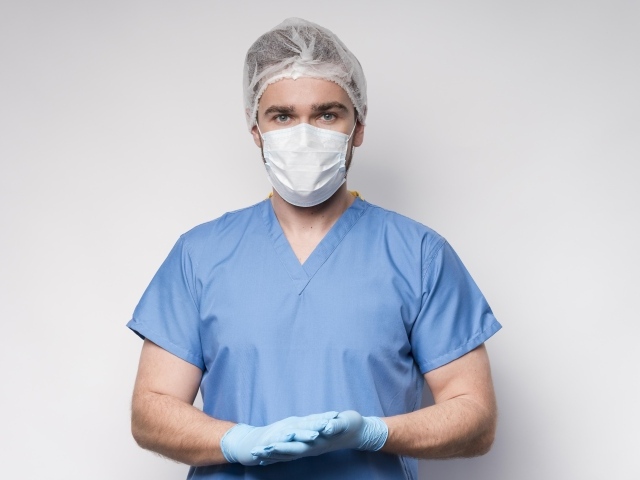 Мужчина врач в маске и перчатках на сером фоне