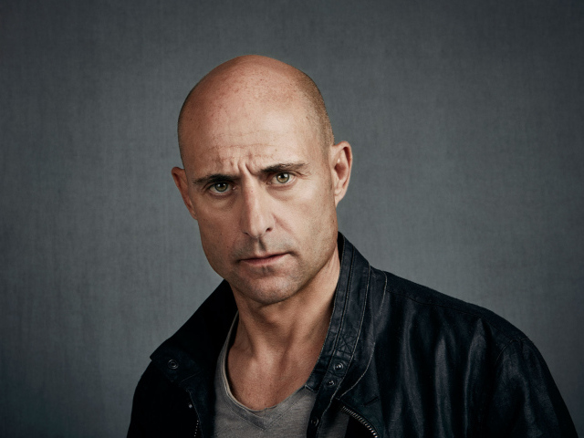 Марк Стронг в черной куртке на сером фоне