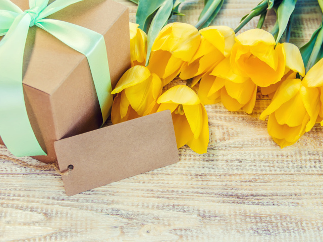 Букет желтых тюльпанов с подарком на столе 